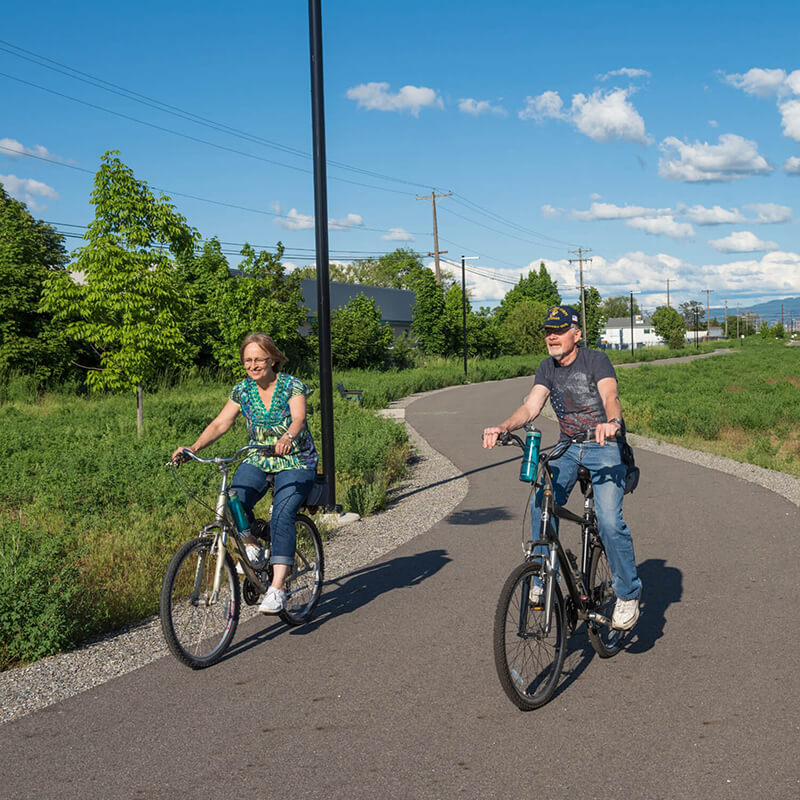A couple riding bicycles together on a paved trail.