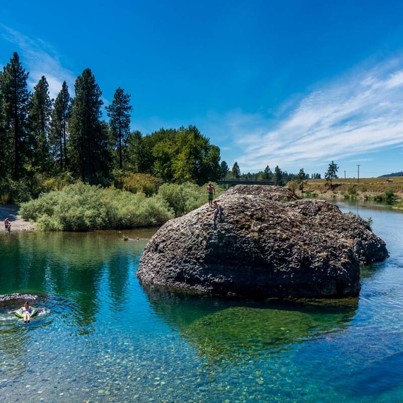 People jumping off a boulder in a river.