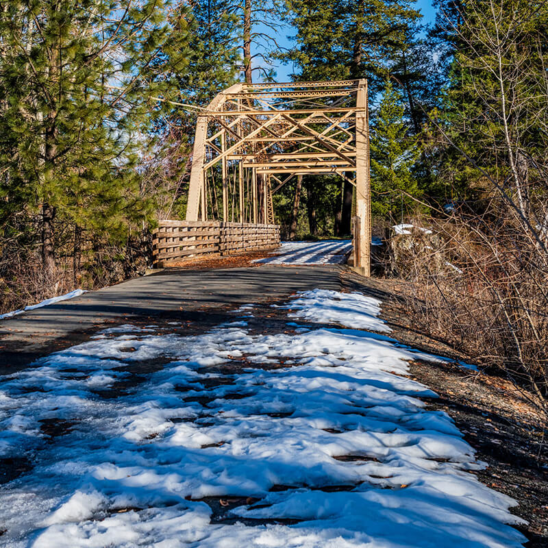 A snowy trail with a small bridge.