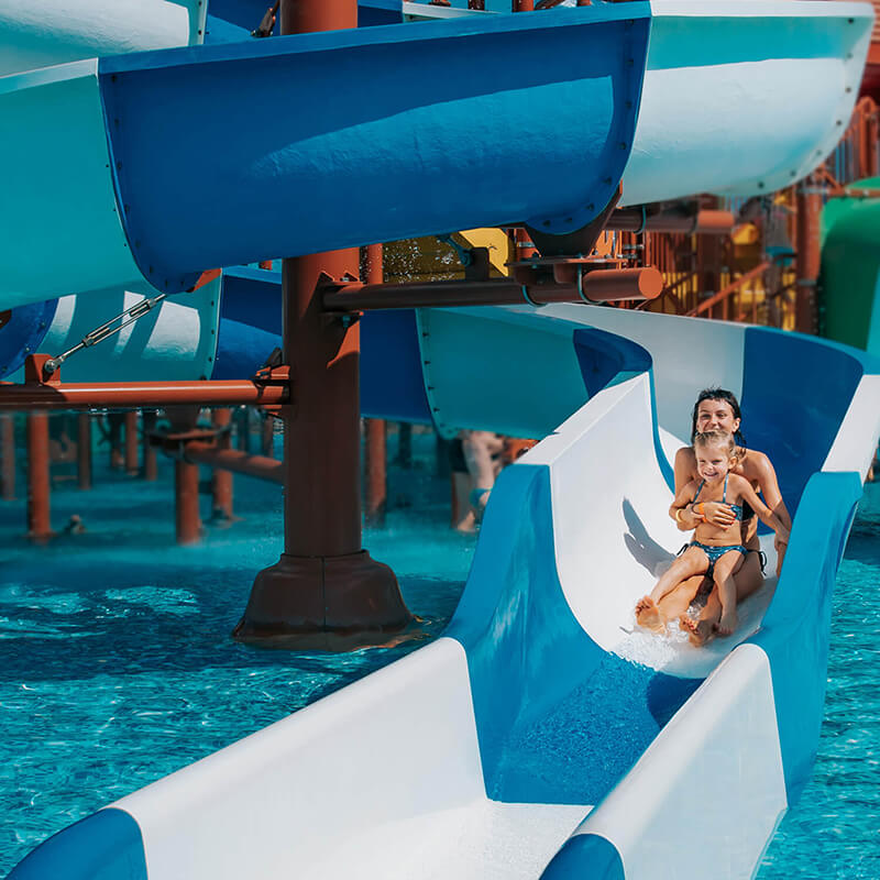 A smiling woman and child sliding down a waterslide.
