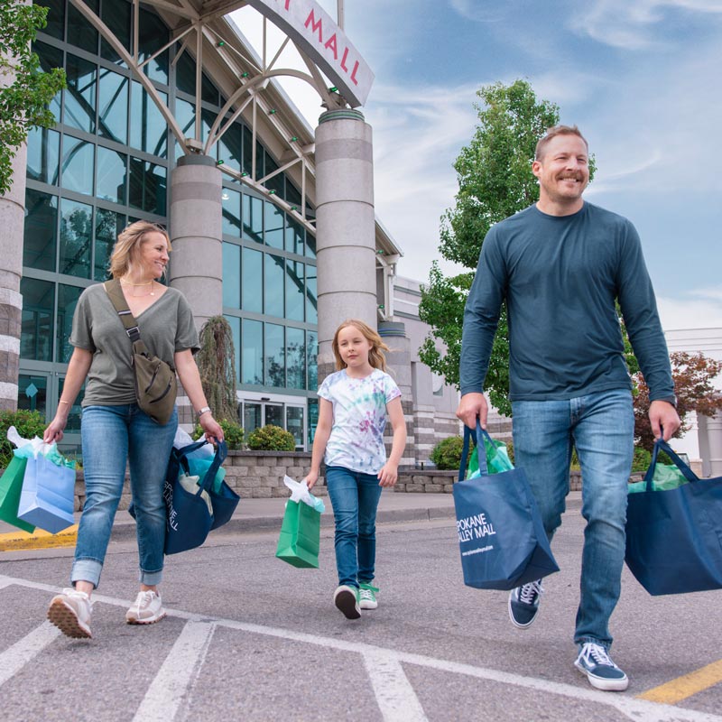 Smiling family walking out from Spokane Valley Mall with full shopping bags.